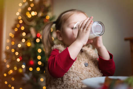 the child eats and drinks milk on the background of a Christmas tree with lights. children's xmas...