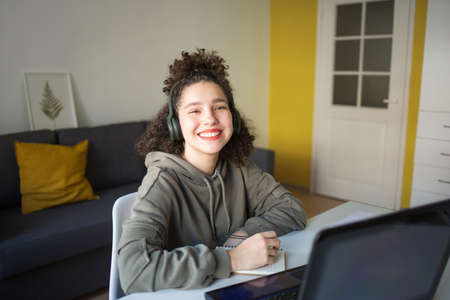 happy mixed rase girl sits at computer screen laptop. student talks over Internet. Video Conference or e-learning at home.の写真素材