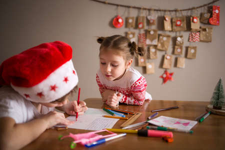 children write letter to Santa Claus at home. sisters girls draw on background of Christmas devoration. concept of new year kids preparation and anticipationの写真素材