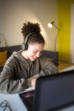 happy mixed rase girl sits at computer screen laptop. student talks over Internet. Video Conference or e-learning at home.の写真素材