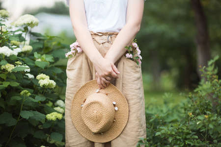 flowers and shrubs in summer Ornamental garden. girl woman in linen skirt and hat on path of Park. Gardening and landscapedの写真素材