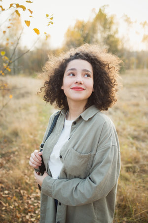portrait of young pretty mixed race teen girl outdoor in autumn. happy woman with finely curly hair in forest or park in autumn.の写真素材