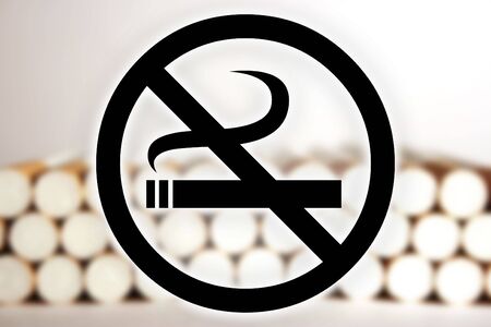 Black "no smoking" sign in front of a blurry picture of cigarettes.の写真素材