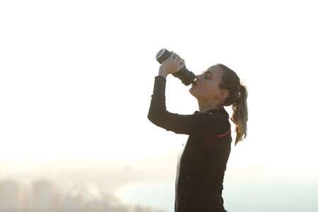 Profile of a runner hydrating drinking water from plastic bottle after exercise outdoorsの写真素材