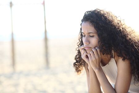 Sad latin girl complaining looking down sitting on the beach