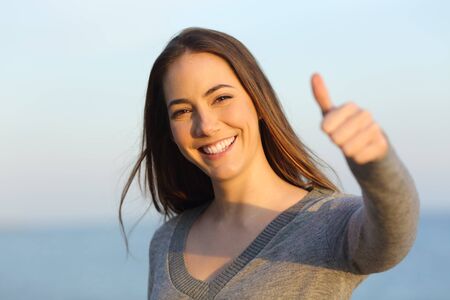 Front view of a happy woman gesturing thumbs up on the beach at sunsetの写真素材