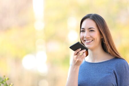 Happy girl recording sms using voice recognition on mobile phone in a park