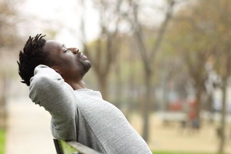 Side view portrait of a black man relaxing sitting on a bench in a parkの写真素材