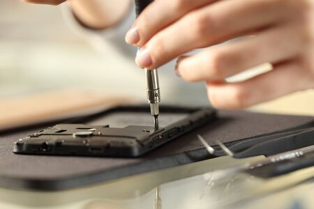 Close up of woman hands removing screws on a smart phone on a desk