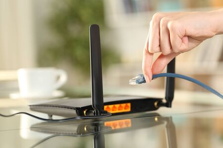 Close up of woman hands plugging network cable to router on a desk at home