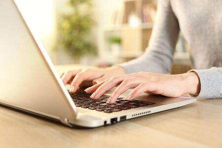 Close up of woman hands typing on laptop sitting on a desk at home