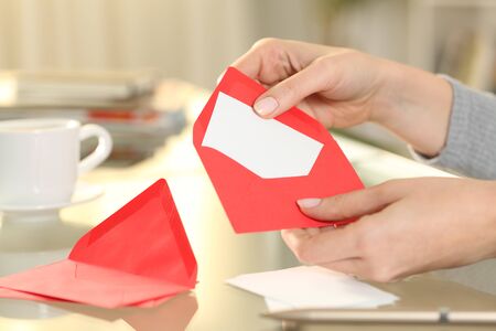 Close up of woman hand putting greeting thank you card on a red envelope sitting on a desk at homeの写真素材