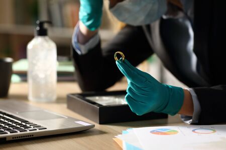 Close up of sad entrepreneur woman holding wedding ring after divorce sitting on a desk at homeofficeの写真素材