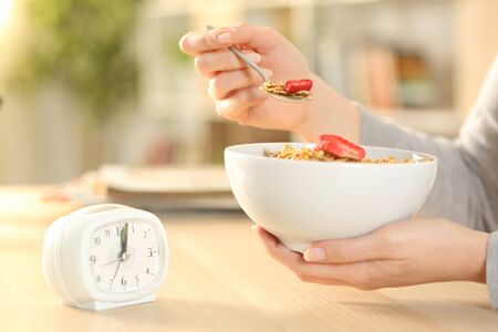 Close up of woman hands eating cereal bowl with fruit after intermittent fasting sitting on a table...