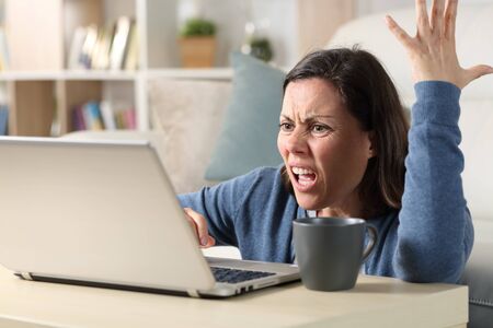 Angry adult woman watching video online on laptop sitting on the floor at homeの写真素材