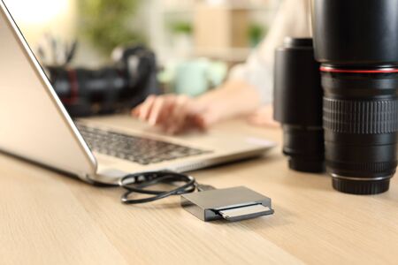 Close up of photographer woman hands transfering files from memory card to laptop on a desk at home