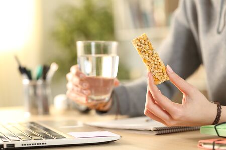 Close up of student hands holding glass of water and snack bar studying at homeの写真素材