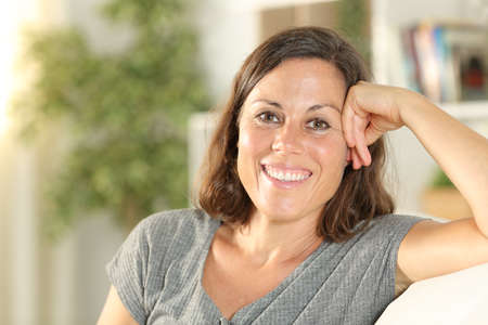 Happy middle age woman posing looking at camera sitting in the sofa at home