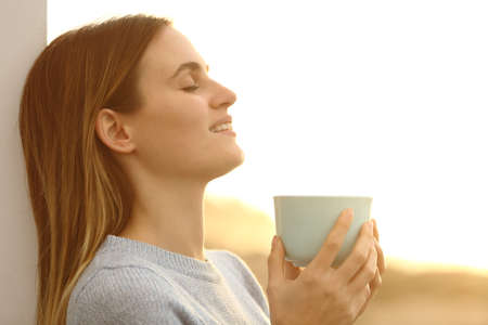 Relaxed woman drinking coffee resting leaing on a wall on the beach at sunset