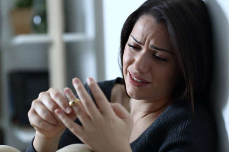 Sad wife complaining and crying touching wedding ring thinking in divorce at home in the night