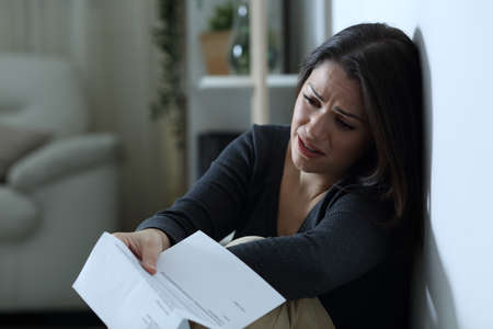 Sad woman complaining after reading a letter sitting on the floor alone at home in the night