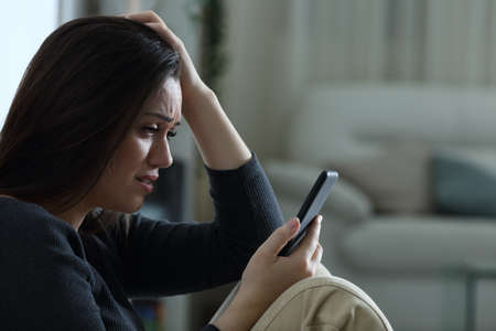 Sad woman reading bad news on mobile phone complaining at home in the night