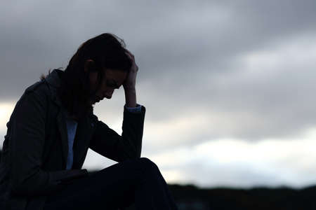 Profile of a sad woman silhouette complaining outdoors on the beachの写真素材