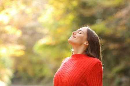 Satisfied woman in red breathing fresh air in autumn in a beautiful forest or parkの写真素材