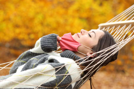 Side view portrait of a lady taking off protective mask to breath fresh air lying on hammockの写真素材