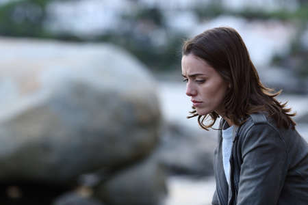 Sad woman sitting alone on the beach complaining looking down