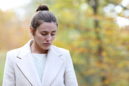 Sad woman walking alone looking down in a park in winter