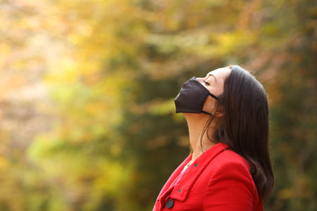 Side view portrait of a woman in red breathing fresh air with mask in a forest in covid times