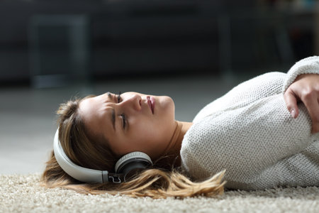 Sad woman listening to music wearing headphones lying on the floor at homeの写真素材