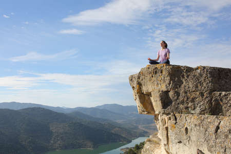 Yogi doing yoga exercise meditating in the top of cliff in the mountain with a beautiful landscape in the backgroundの写真素材