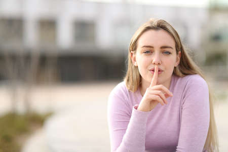 Front view of a teen female asking for silence with finger on lips outdoor in the streetの写真素材