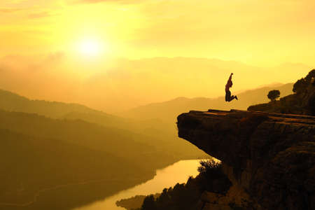 Backlight of a happy woman silhouette jumping in the mountain on vacation at sunsetの写真素材