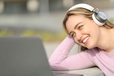 Happy teen wearing headphones watching and listening media on laptop in a parkの写真素材