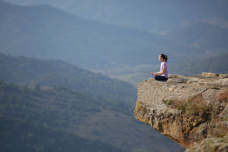 Woman practicing yoga exercise meditating in the top of a cliff in the mountainの写真素材