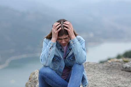 Sad single teenager female complaining in a cliff in the mountainの写真素材
