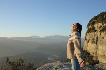 Side view of a woman in sweater breathing fresh air in the mountain in winterの写真素材