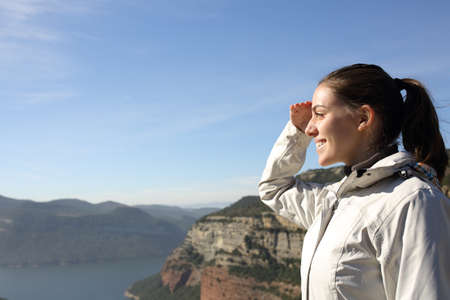 Side view portrait of a happy trekker contemplating views with hand on forehead in the mountain on...