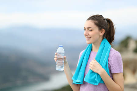 Happy jogger holding a bottle of water contemplating views after sport in the mountain
