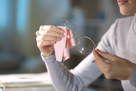 Close up of a woman hands cleaning eyeglasses in the night at homeの写真素材