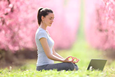 Happy yogi e-learning yoga watching video tutorials on laptop in a pink flowered field in springの写真素材
