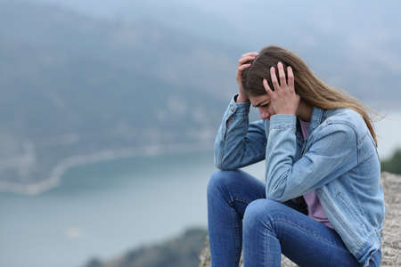 Sad teen complaining sitting alone in a cliff in the mountainの写真素材