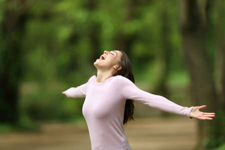Excited woman outstretching arms and screaming in a forest celebrating vacation