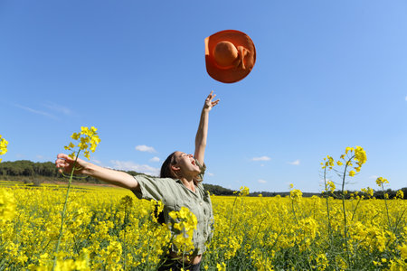 Happy woman throwing pamela celebrating vacation in a yellow flowered field in springの写真素材
