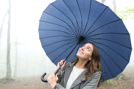 Happy woman under umbrella looking at the rain walking in a foggy park