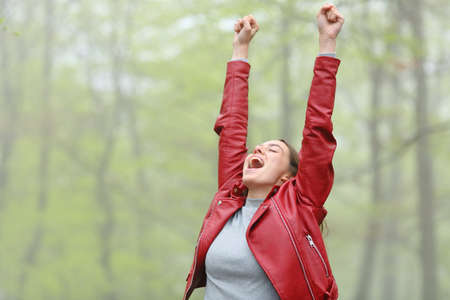 Woman in red excited raising arms screaming in a forestの写真素材
