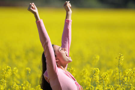 Side view portrait of an excited woman raising arms in a yellow field in spring seasonの写真素材